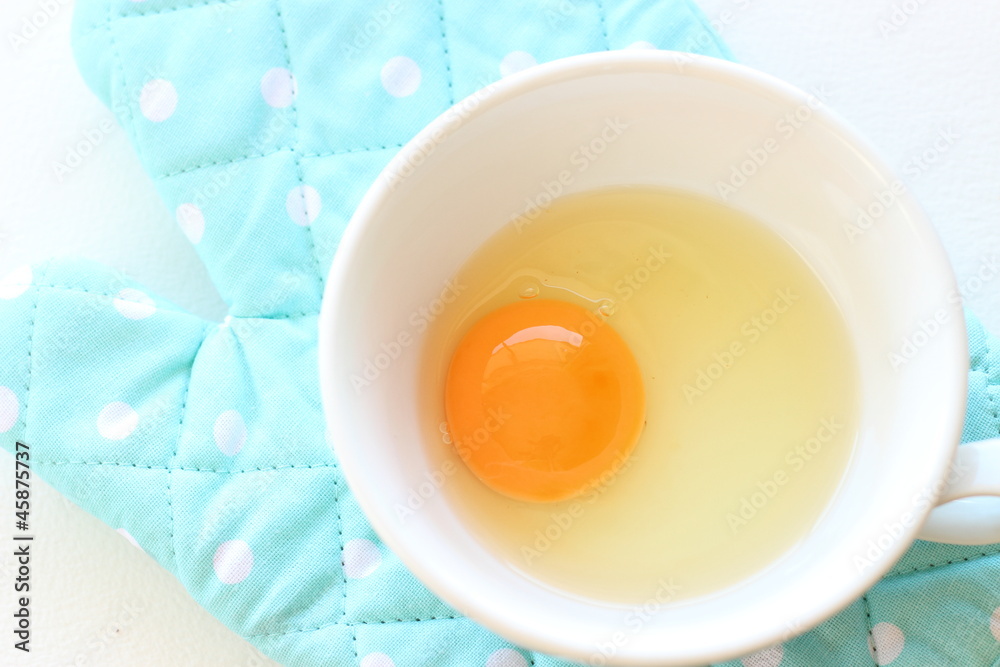Fresh raw egg in soup cup with blue oven mitt Fresh raw egg in soup cup with blue oven mitt