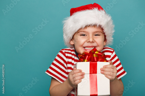 Funny child in Santa red hat holding Christmas gift in hand.