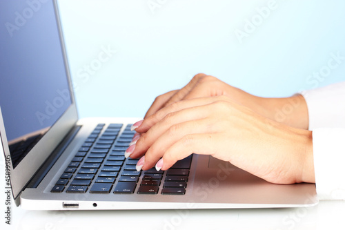 Hands typing on laptop keyboard close up on blue background