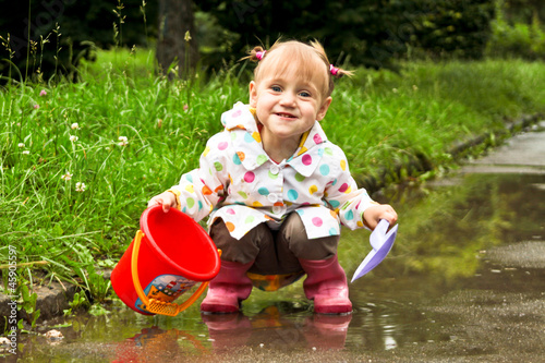 cute little girl is playing in muddy puddles