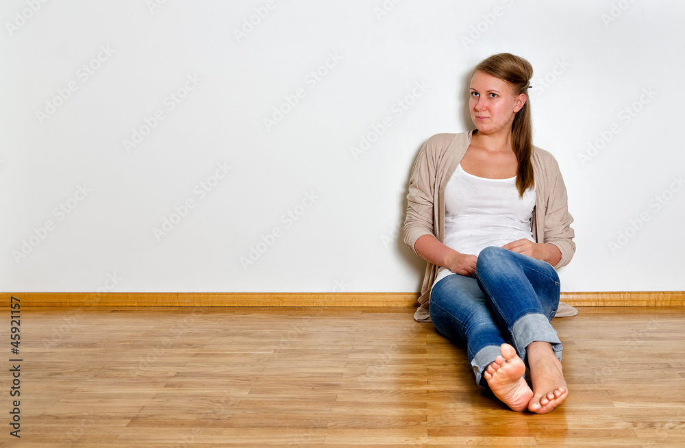 Young woman sitting on the wooden floor against white wall Young woman sitting on the wooden floor against white wall
