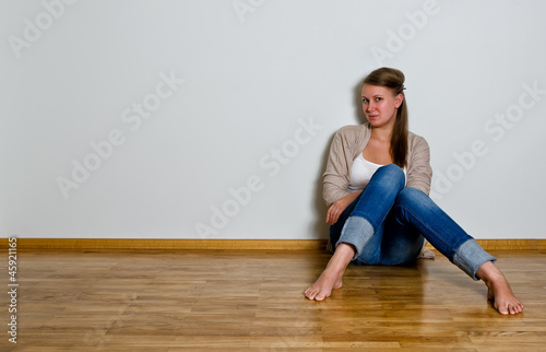 Young woman sitting on the wooden floor against white wall