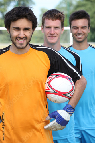 Three smiling footballers with ball