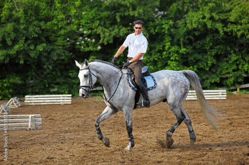 Jockey in glasses rides horse near barrier on hippodrome