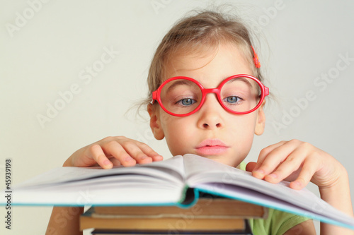 Little girl in red glasses read book