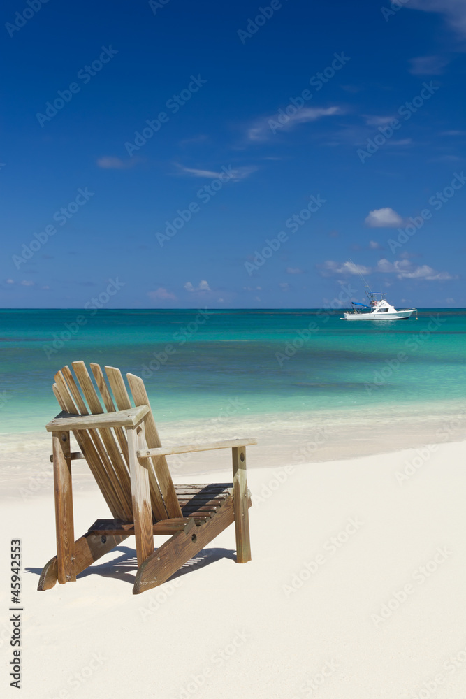 Beach chair on sandy beach with white boat on background