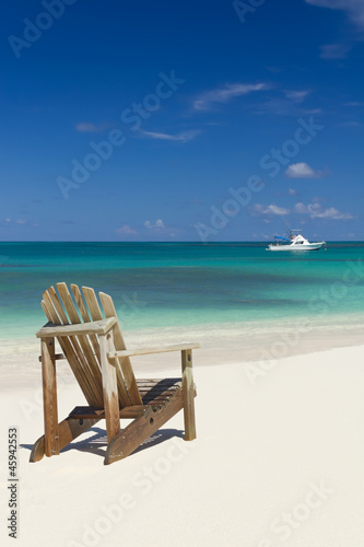 Beach chair on sandy beach with white boat on background