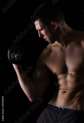Strong muscular sports man rising dumbbell on black