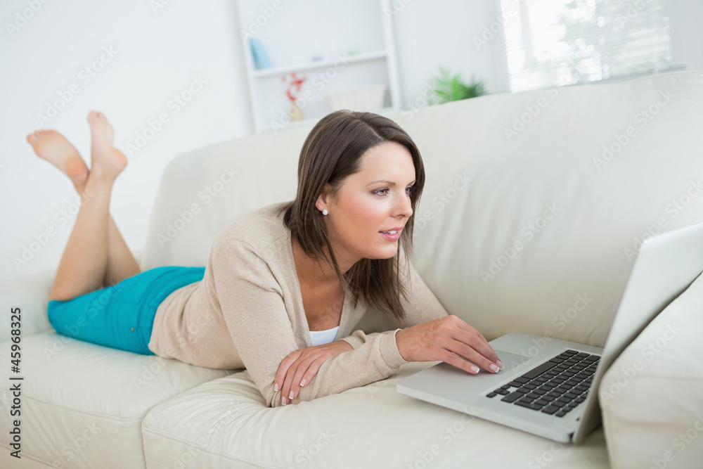 Brunette lying on sofa and using her laptop Brunette lying on sofa and using her laptop