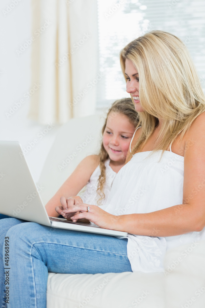 Woman typing on notebook while her daughter is sitting next to h Woman typing on notebook while her daughter is sitting next to h
