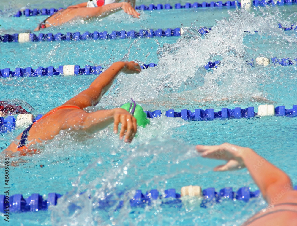 Female swimmers in a close butterfly race at an outdoor pool