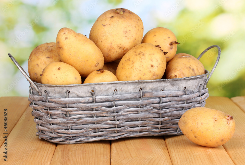 Ripe potatoes on basket on wooden table on natural background Ripe potatoes on basket on wooden table on natural background