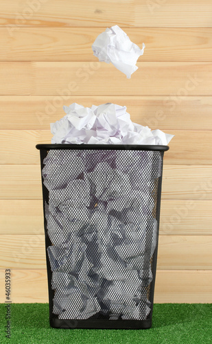 metal trash bin from paper on grass on wooden background