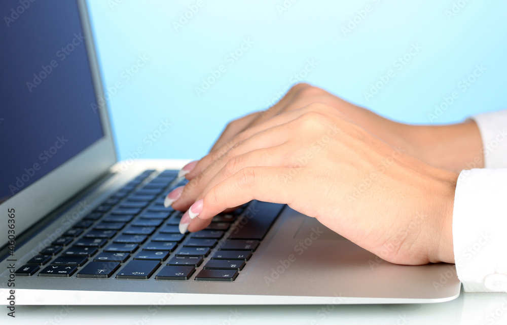 Hands typing on laptop keyboard close up on blue background Hands typing on laptop keyboard close up on blue background