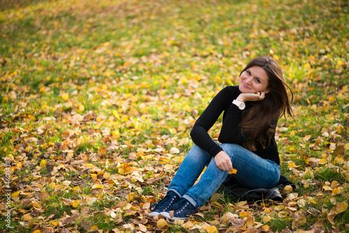 young woman sits on leaves in autumn park