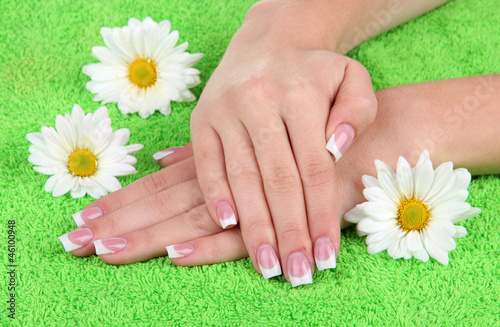 Woman hands with french manicure and flowers on green towel