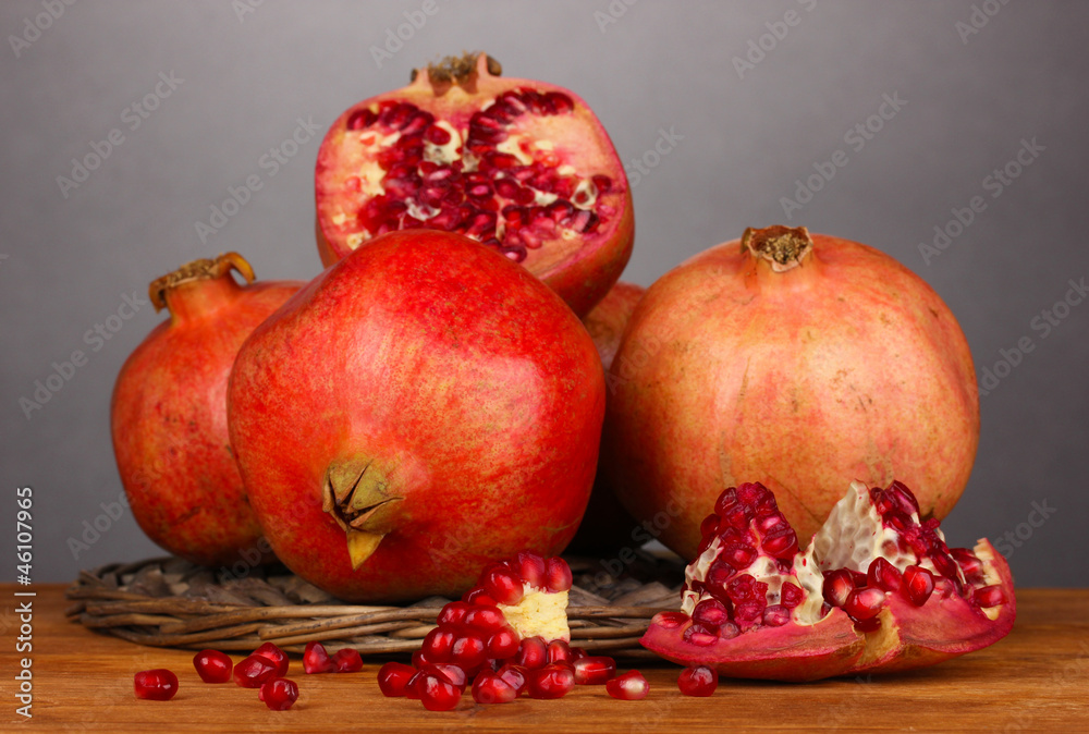 Ripe pomegranates on wicker cradle on grey background Ripe pomegranates on wicker cradle on grey background
