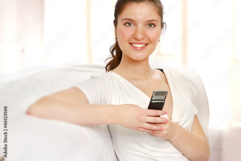 A smiling woman with a mobile phone on a sofa indoors A smiling woman with a mobile phone on a sofa indoors
