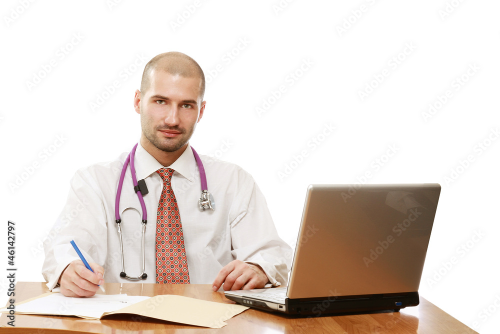 A male doctor is sitting and writing in front of a laptop