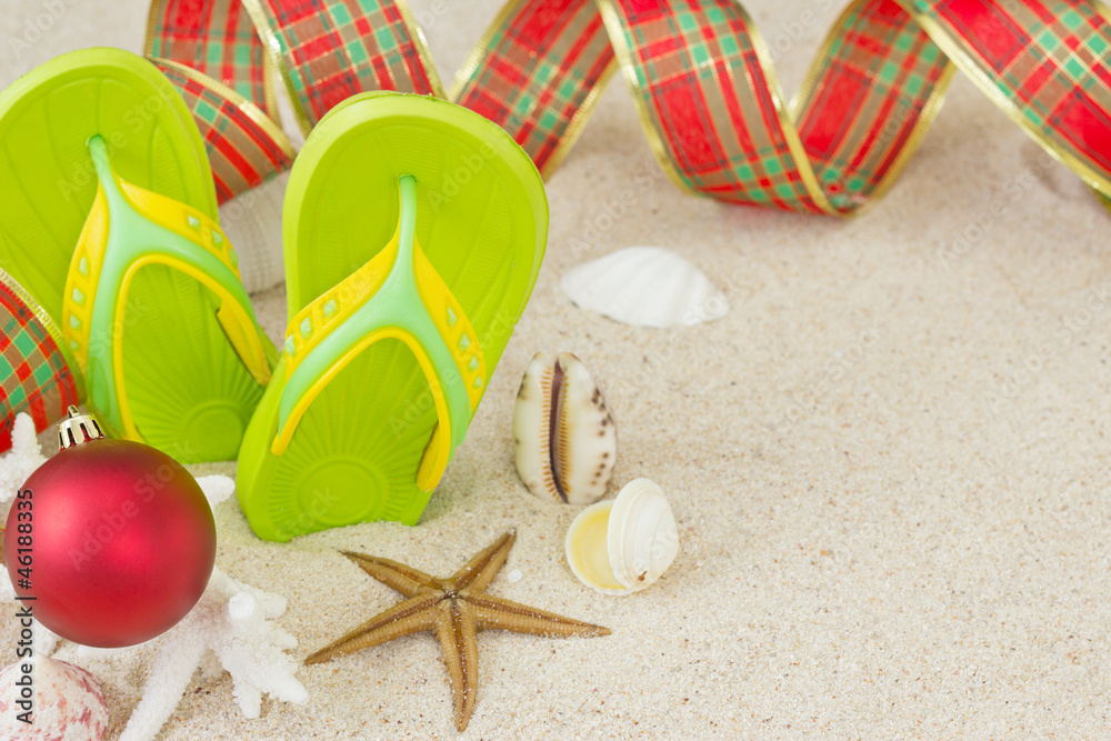 Flip Flops in the sand with shells and Christmas decoration.