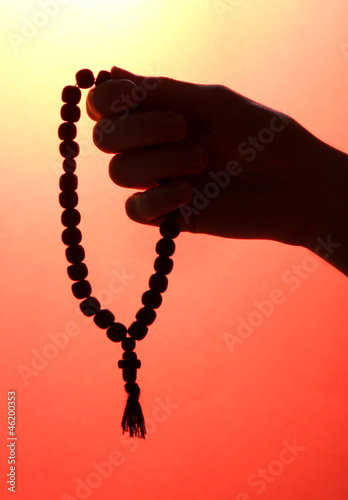 male hand with rosary, on red background