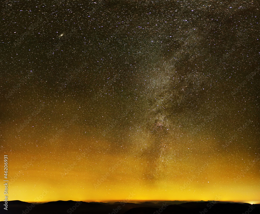Milky way over black mountains and city lights