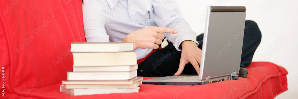 Junge liegt auf der Couch mit Büchern und Laptop