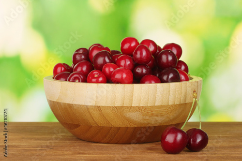 cherry in wooden bowl on wooden table on green background