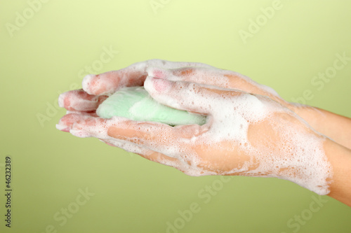 Woman s hands in soapsuds  on green background close-up
