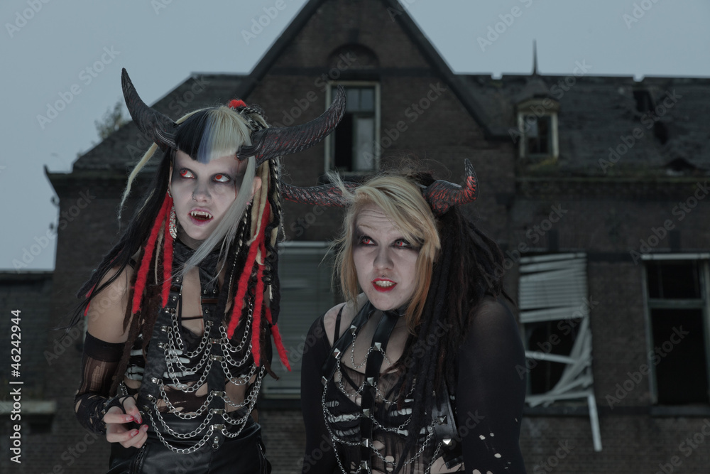 Two scary hungry female demons in front of spooky house.