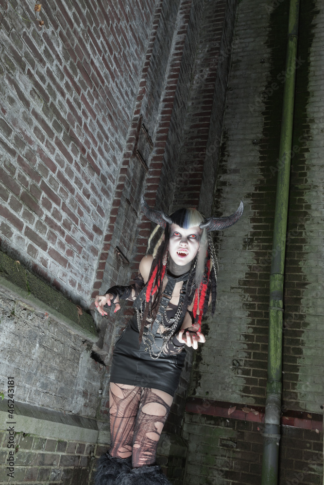 Naklejka premium Scary female demon in front of old dirty brick wall.
