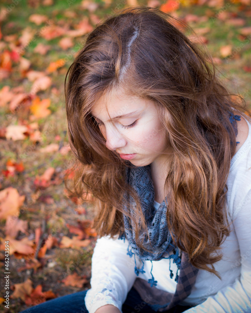 Naklejka premium lonely teenage girl sitting quietly in fall leaves