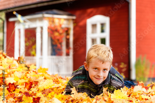 Blonder Junge im Herbstlaub vor Schwedenhaus liegend photo