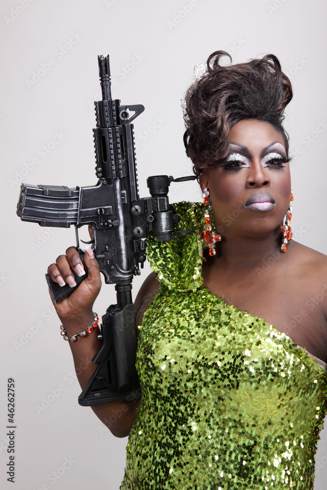 Drag queen wearing a green gown holding an assault rifle. Stock Photo