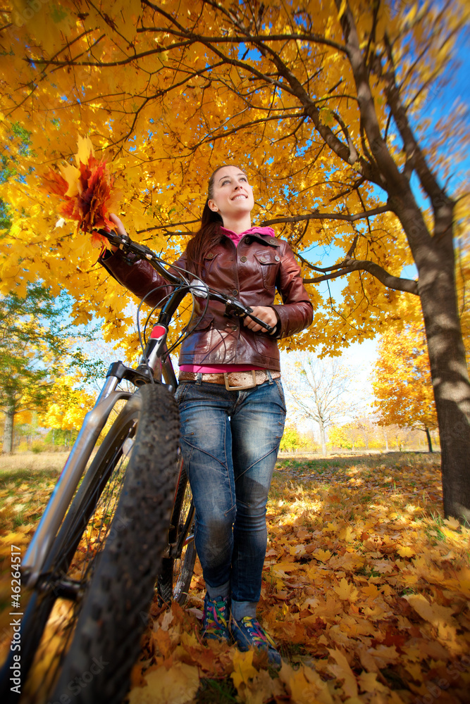 woman with bike on a yellow autumn leafs background
