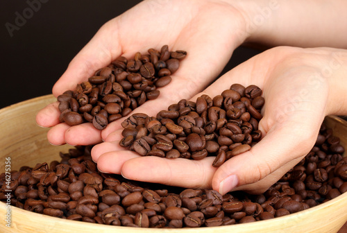 Coffee beans in hands on dark background