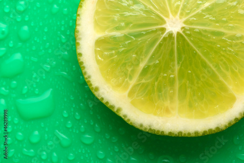 Slice of lime with drop on green background