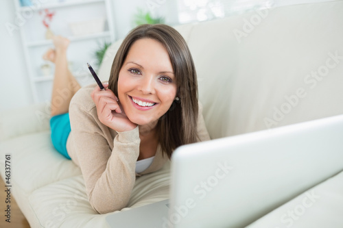 smiling woman using her laptop lying on sofa