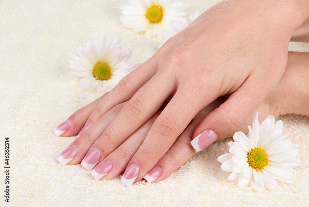 Woman hands with french manicure and flowers on towel Woman hands with french manicure and flowers on towel