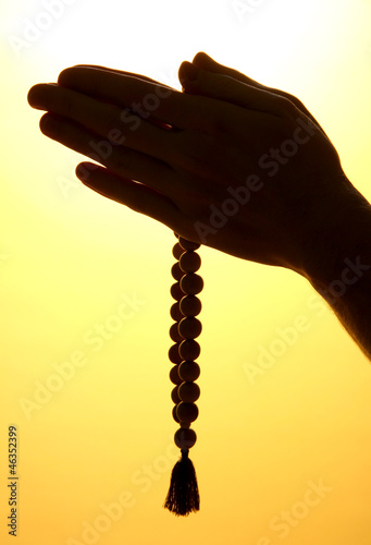 male hands with rosary, on yellow background