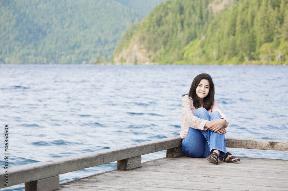 Young teen girl sitting quietly on lake pier, relaxing