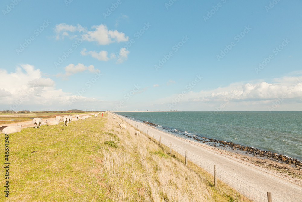 Dutch wide landscape with dike and blue cloudy sky.