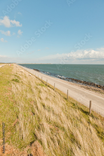 Dutch wide landscape with dike and blue cloudy sky.