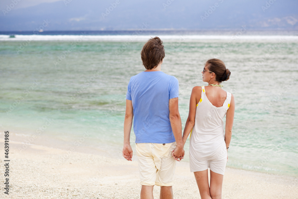 back view of happy young couple holding hands on the beach. hone
