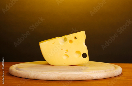 Cheese on cutting board on wooden table on brown background