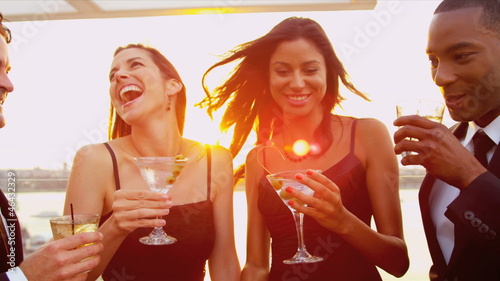 Diverse friends enjoying cocktails and fun at sunset party dressed in black  photo