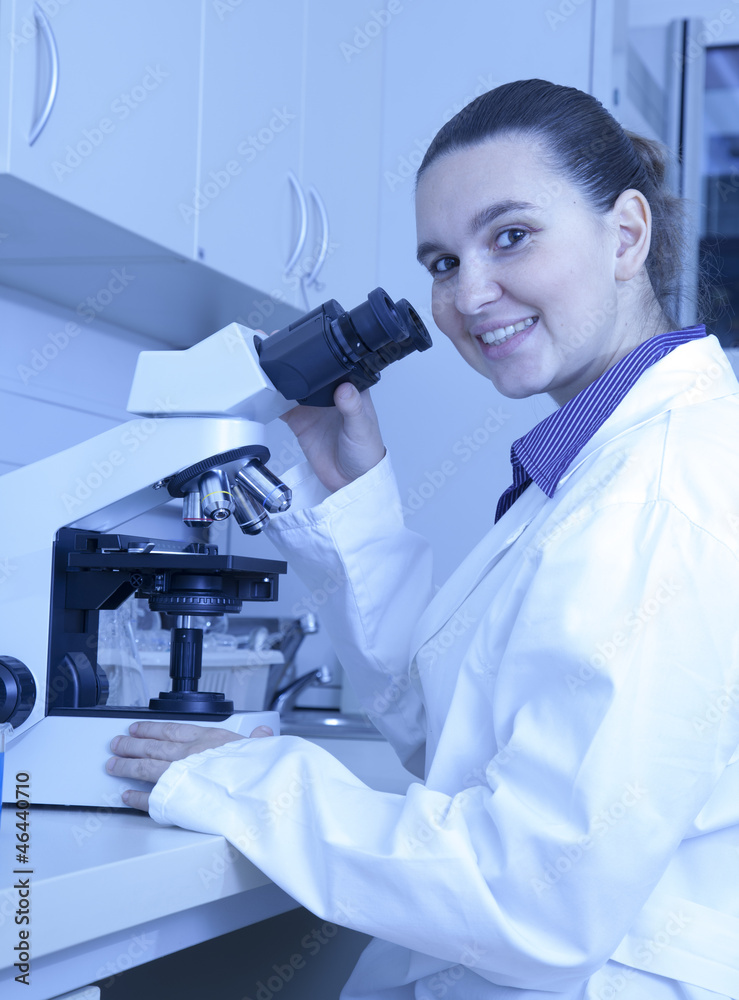 Cute smiling female medical researcher using her microscope Cute smiling female medical researcher using her microscope