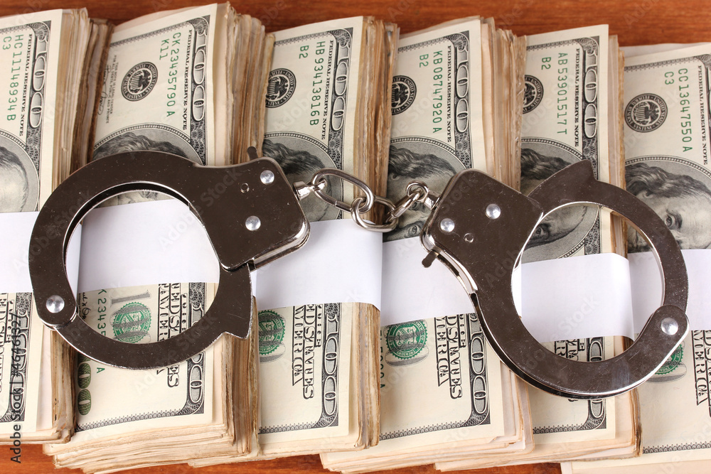 Handcuffs on the packs of dollars on wooden table close-up Handcuffs on the packs of dollars on wooden table close-up