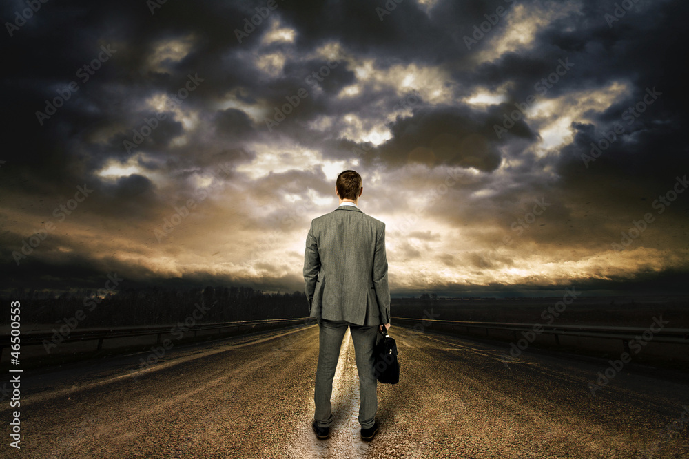 Business man standing in the middle of the road. Dramatic sky ab Business man standing in the middle of the road. Dramatic sky ab