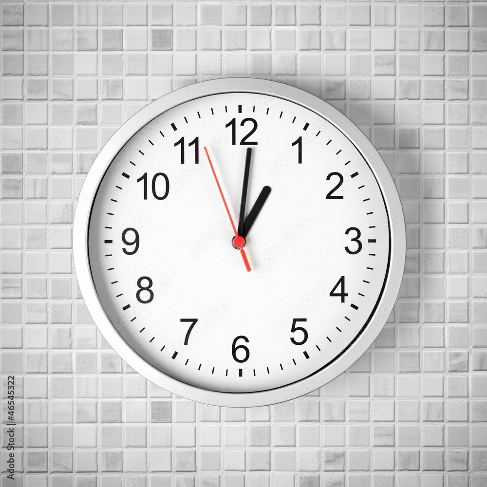 Simple clock or watch on white tile wall displaying one o'clock Stock